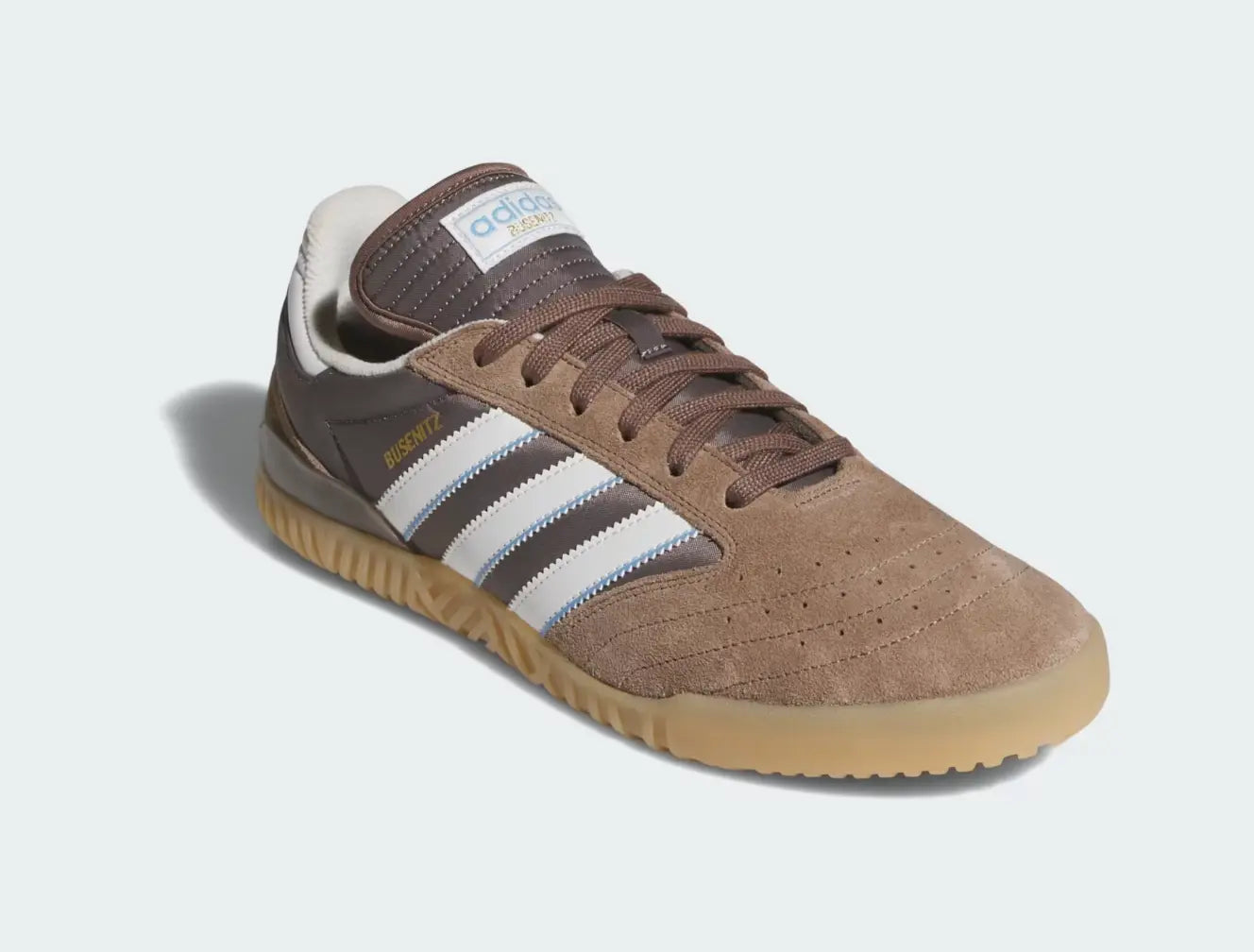 Chaussure de skate marron en suède par Adidas, avec trois bandes blanches et bleues, et semelle extérieure en caoutchouc.