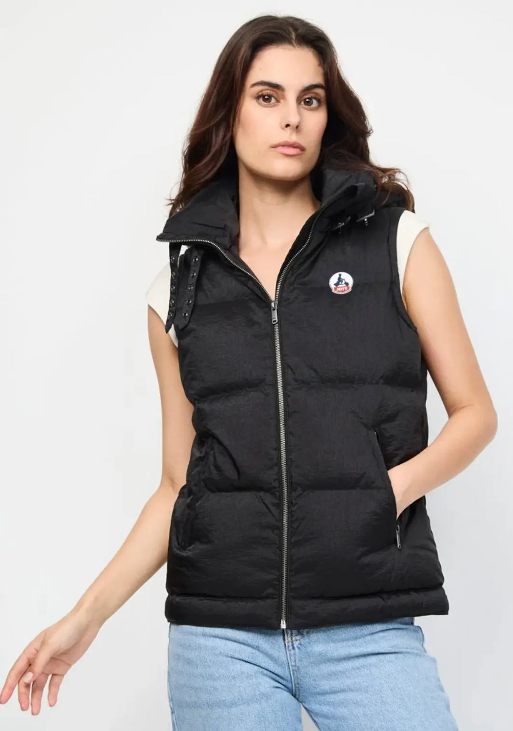 Veste sans manches noire de JOTT avec col montant et poches zippées, portée avec un t-shirt blanc et un jean clair.