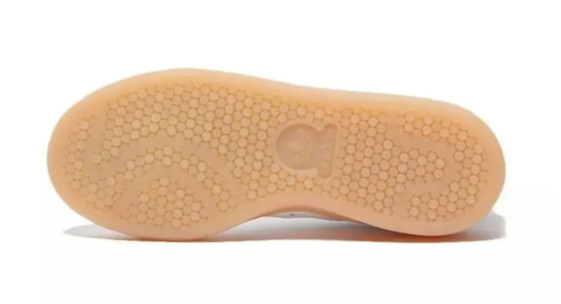 Semelle en caoutchouc beige d'une Adidas Stan Smith, avec motif hexagonal répété et logo de la marque.