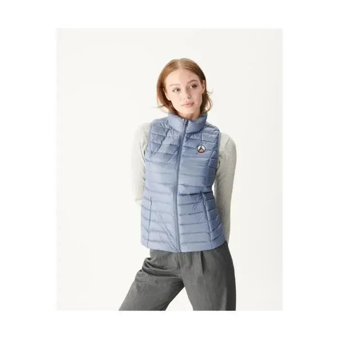 Doudoune sans manches bleue de Jott, portée sur un pull gris, et un pantalon gris foncé.