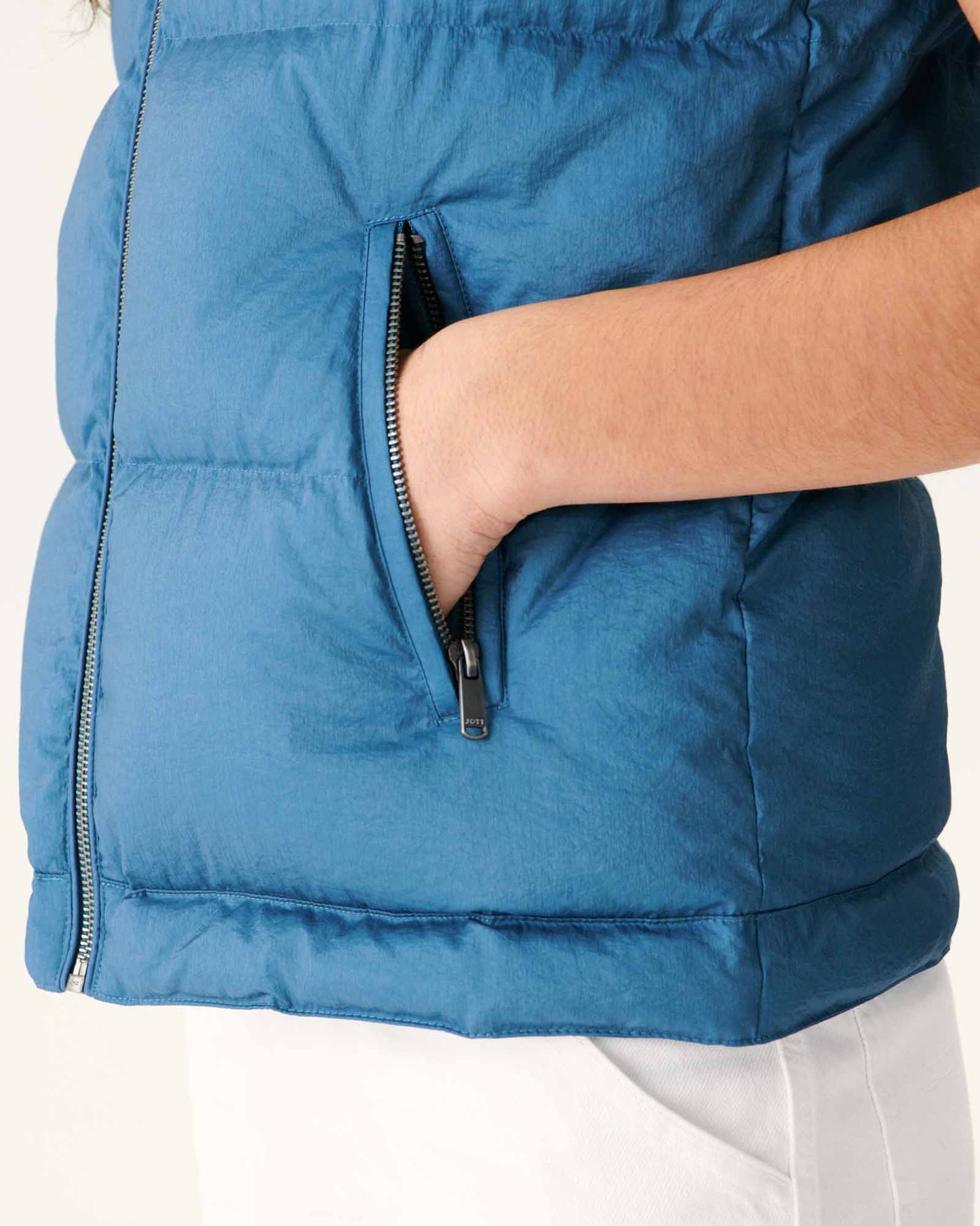 Doudoune sans manches bleue Jeans de Jott, avec fermeture éclair visible et une main dans la poche.