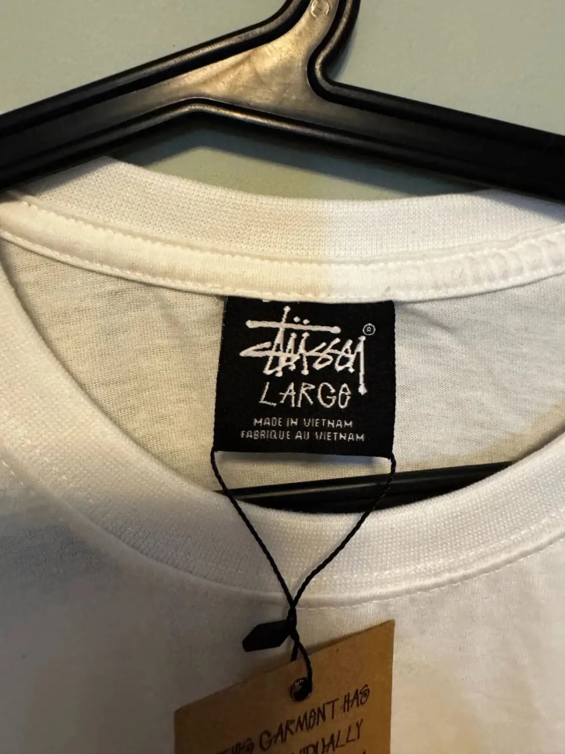 T-shirt blanc par Stüssy, étiquette noire de la marque visible, suspendu sur un cintre noir.