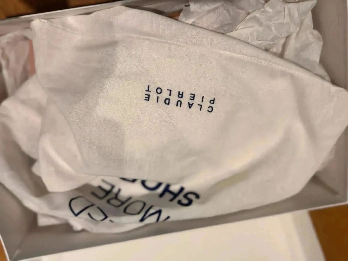 Pochette de protection blanche pour chaussures de Claudie Pierlot, avec du papier de soie visible.