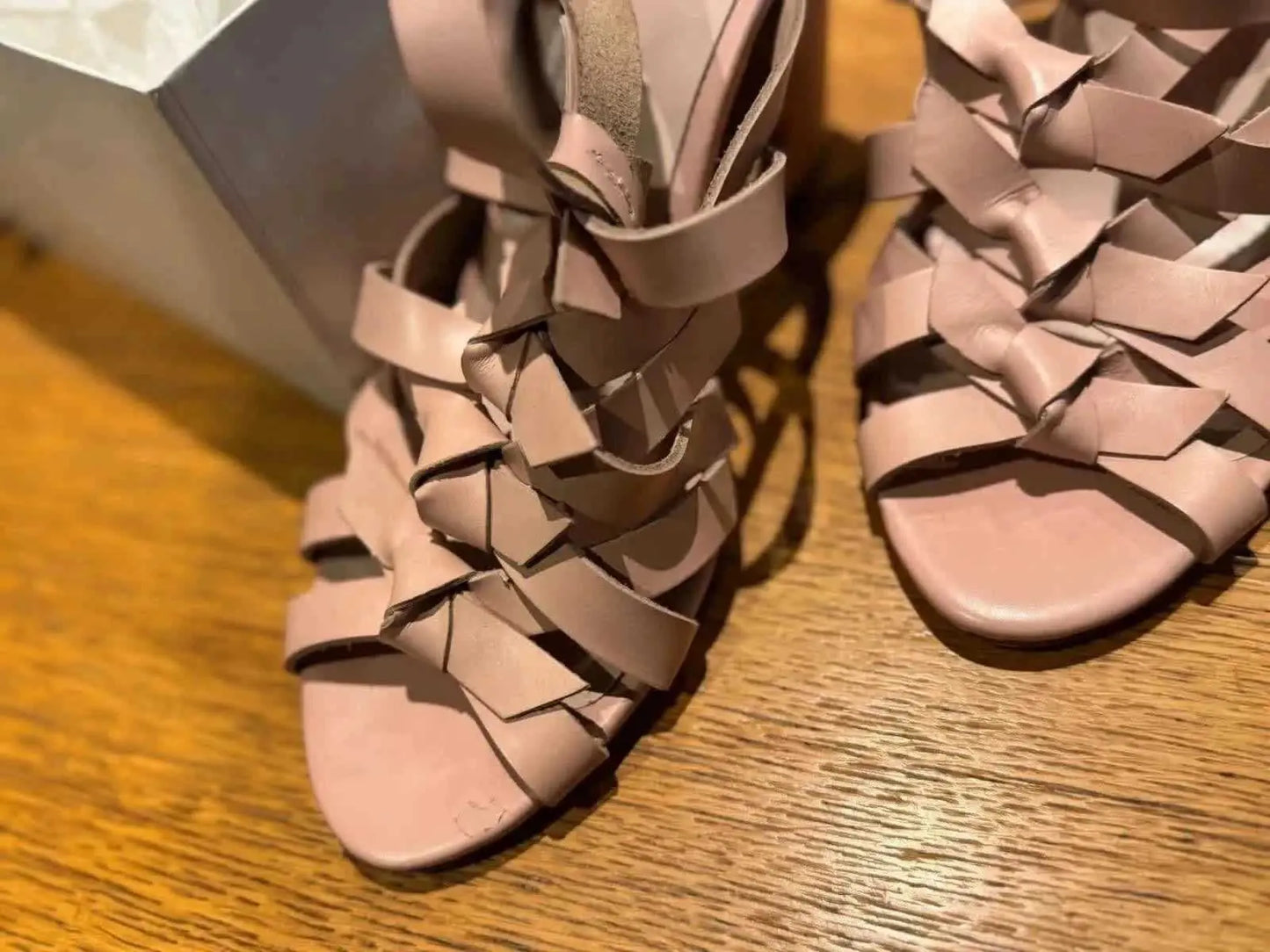 Sandales roses poudré de Claudie Pierlot, à brides en cuir tressées, présentées sur un parquet en bois.