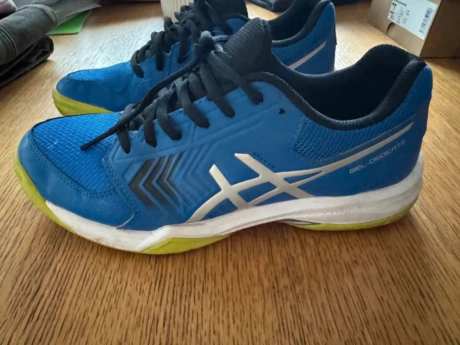 Chaussures de sport bleues de ASICS, avec semelles blanches et détails argentés, présentées sur une surface en bois.