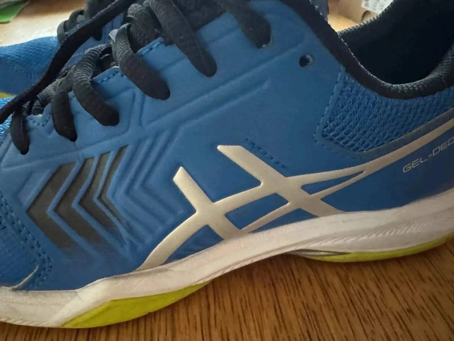 Chaussure de sport bleue, de Asics, avec rayures décoratives sur le côté et semelle jaune et blanche.