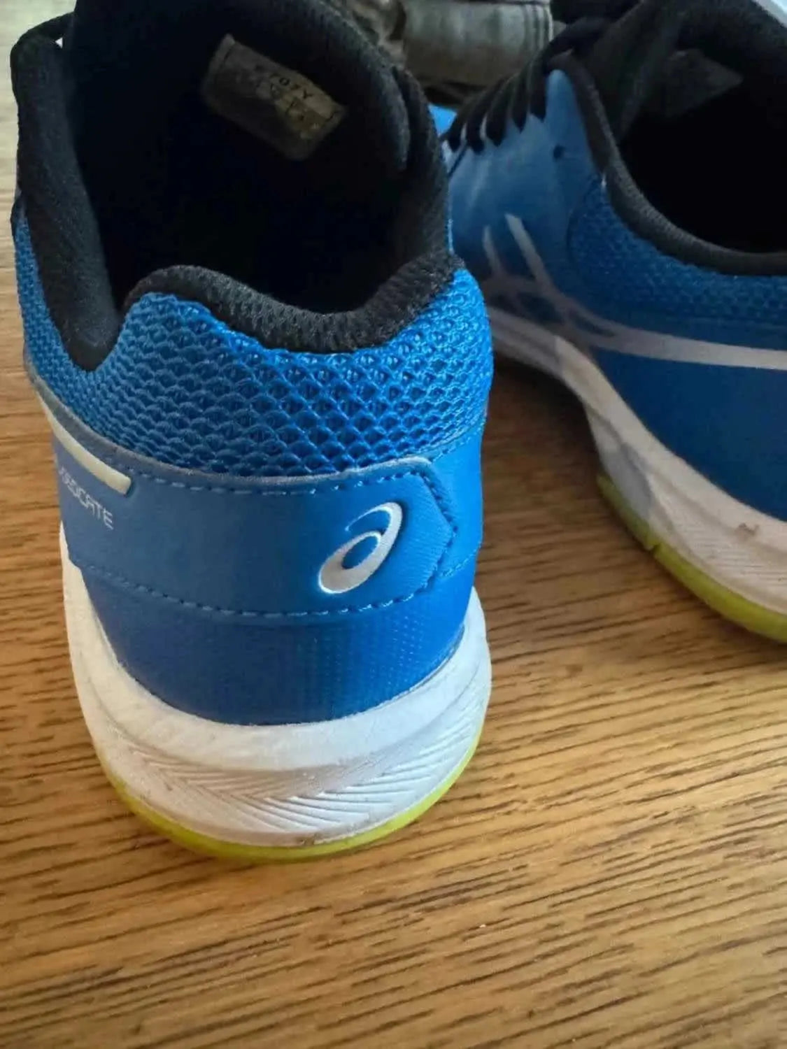 Chaussure de sport bleue par ASICS, détail du logo, texture en maille sur le dessus, et semelle blanche à bande jaune.