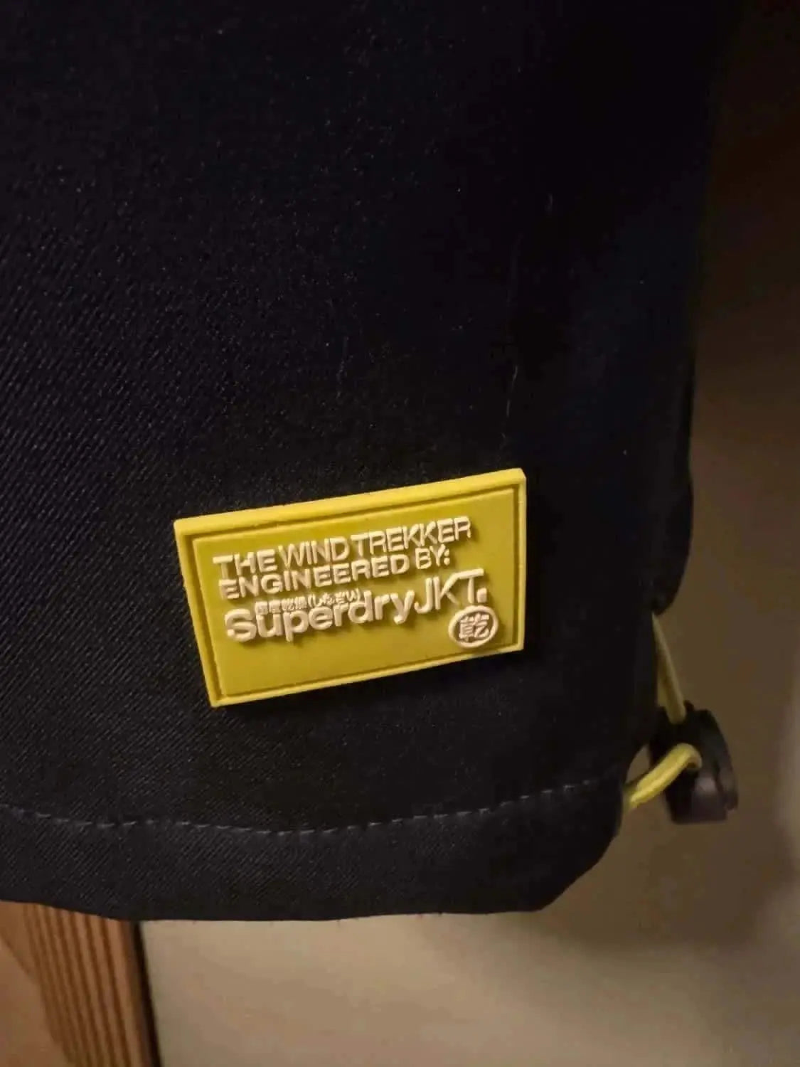 Veste noire de Superdry Windtrekker, avec un écusson jaune portant le logo de la marque.