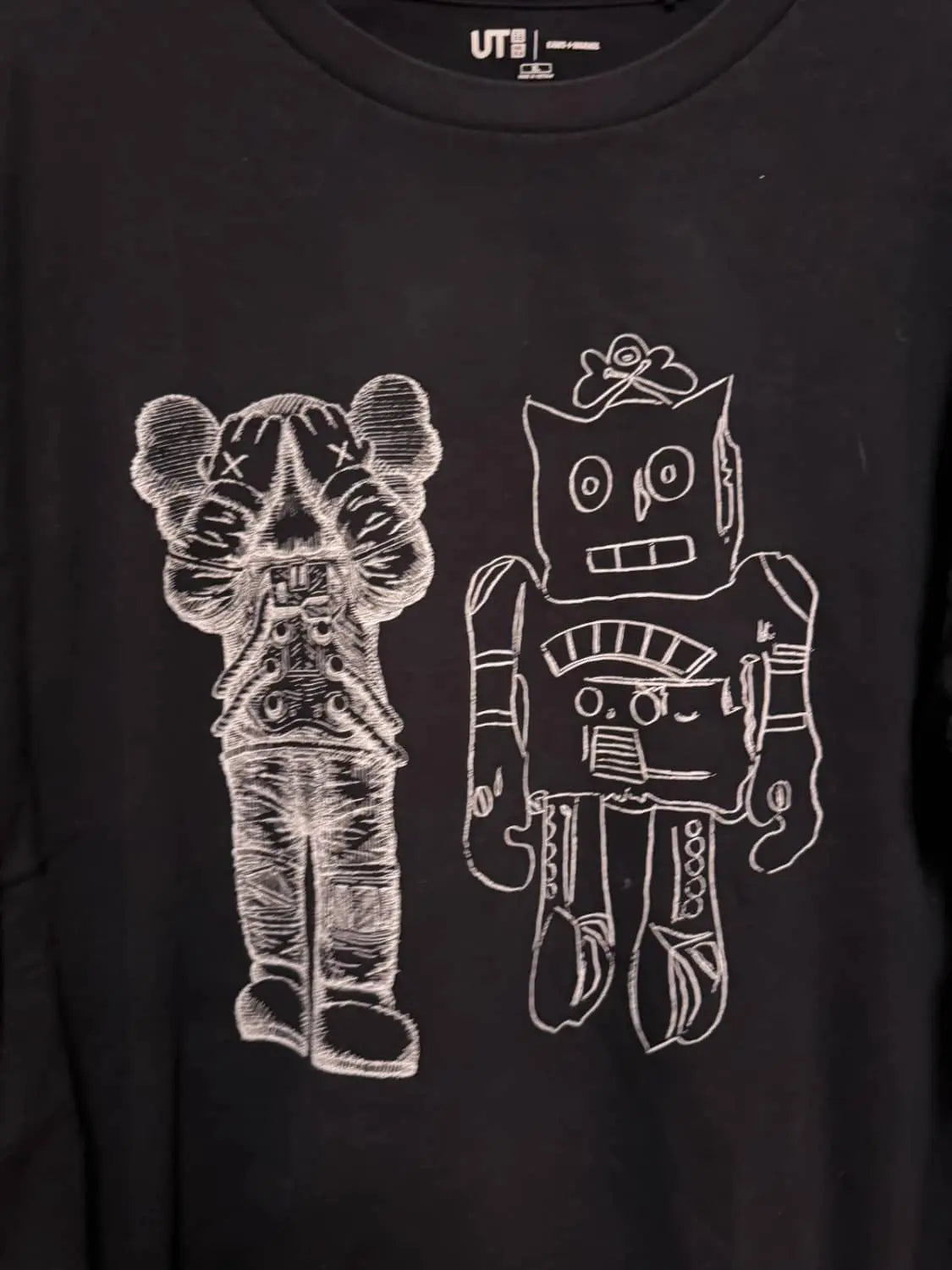 T-shirt noir de Uniqlo, collaboration avec KAWS et Andy Warhol, orné de motifs graphiques blancs.