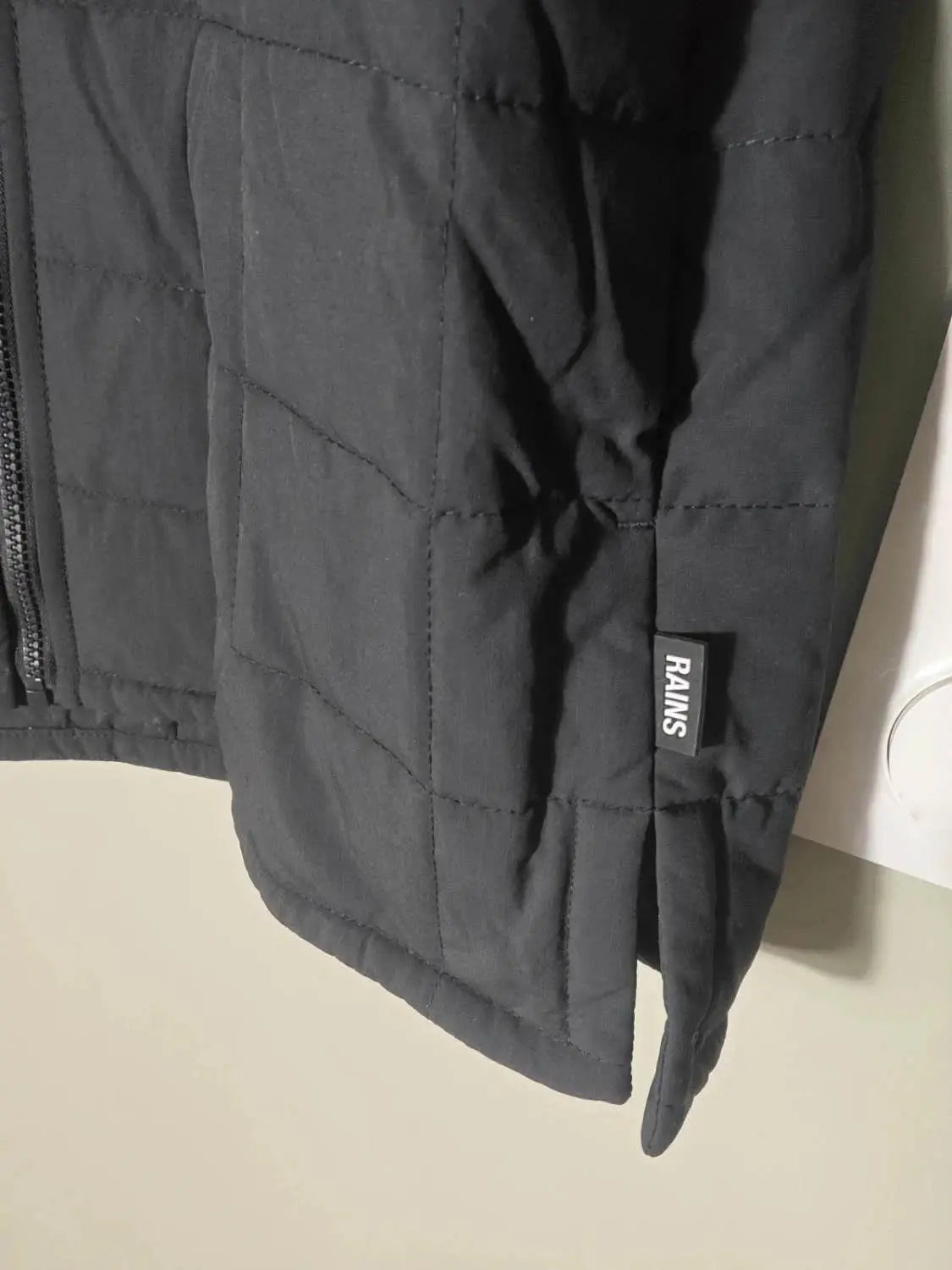 Veste matelassée noire de Rains, avec une fermeture éclair et un ourlet fendu.