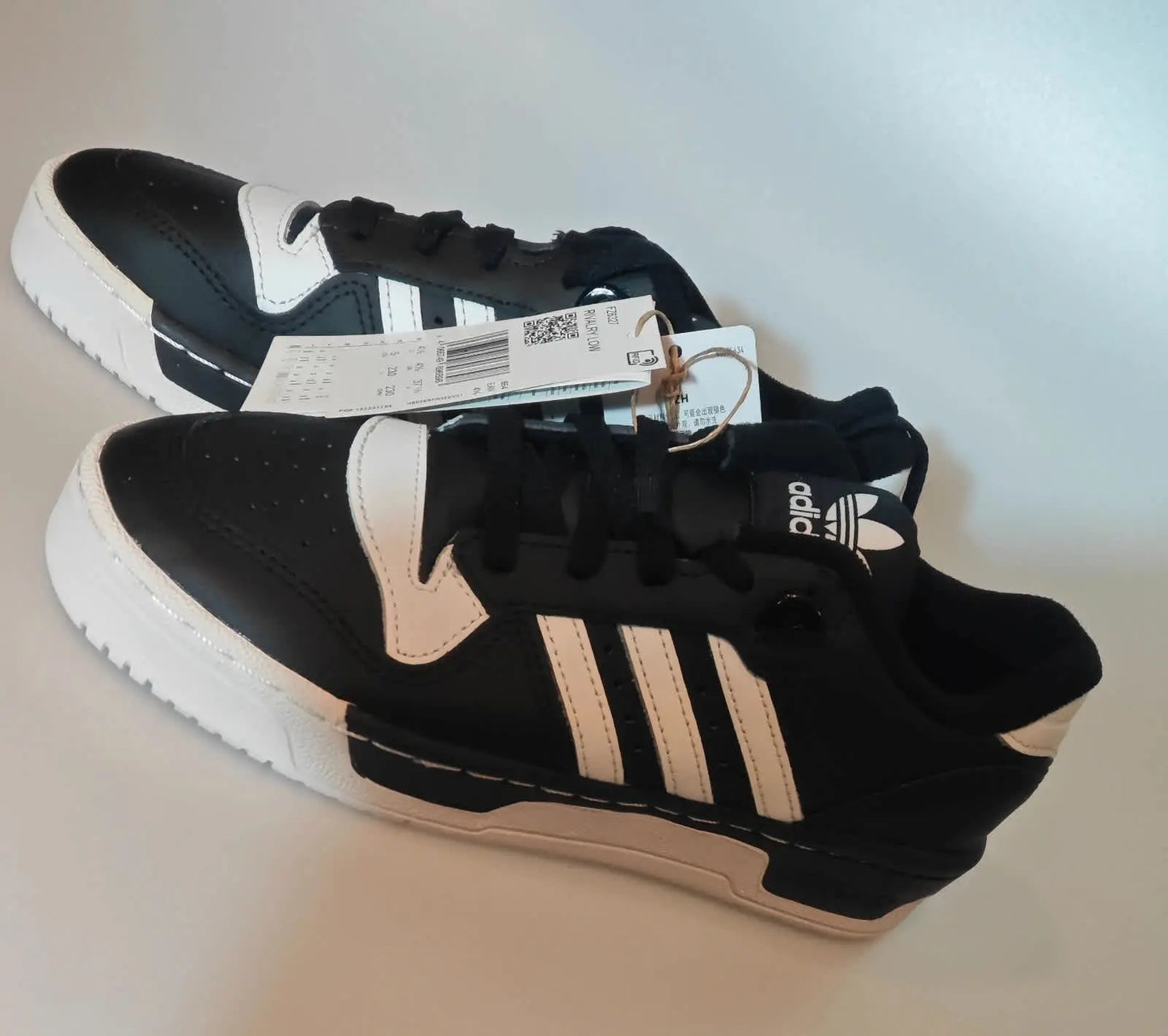 Baskets basses noires et blanches Adidas Rivalry Low de Adidas, présentées avec leur étiquette.