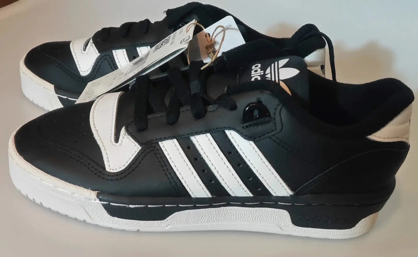 Baskets basses noires et blanches de Adidas, avec trois rayures blanches sur le côté.