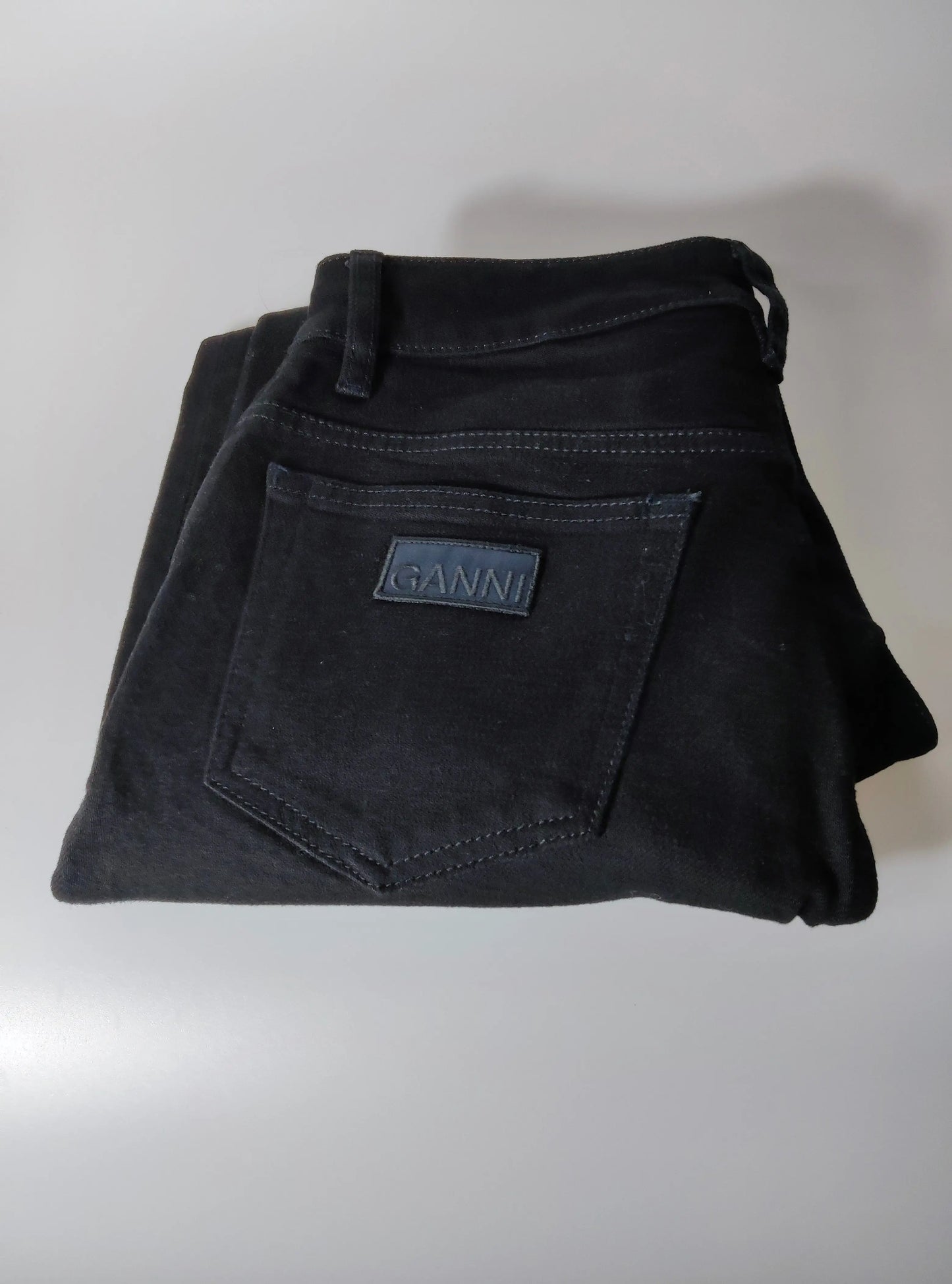 Jean noir cropped taille haute en coton bio de Ganni, plié avec étiquette logo sur la poche arrière.
