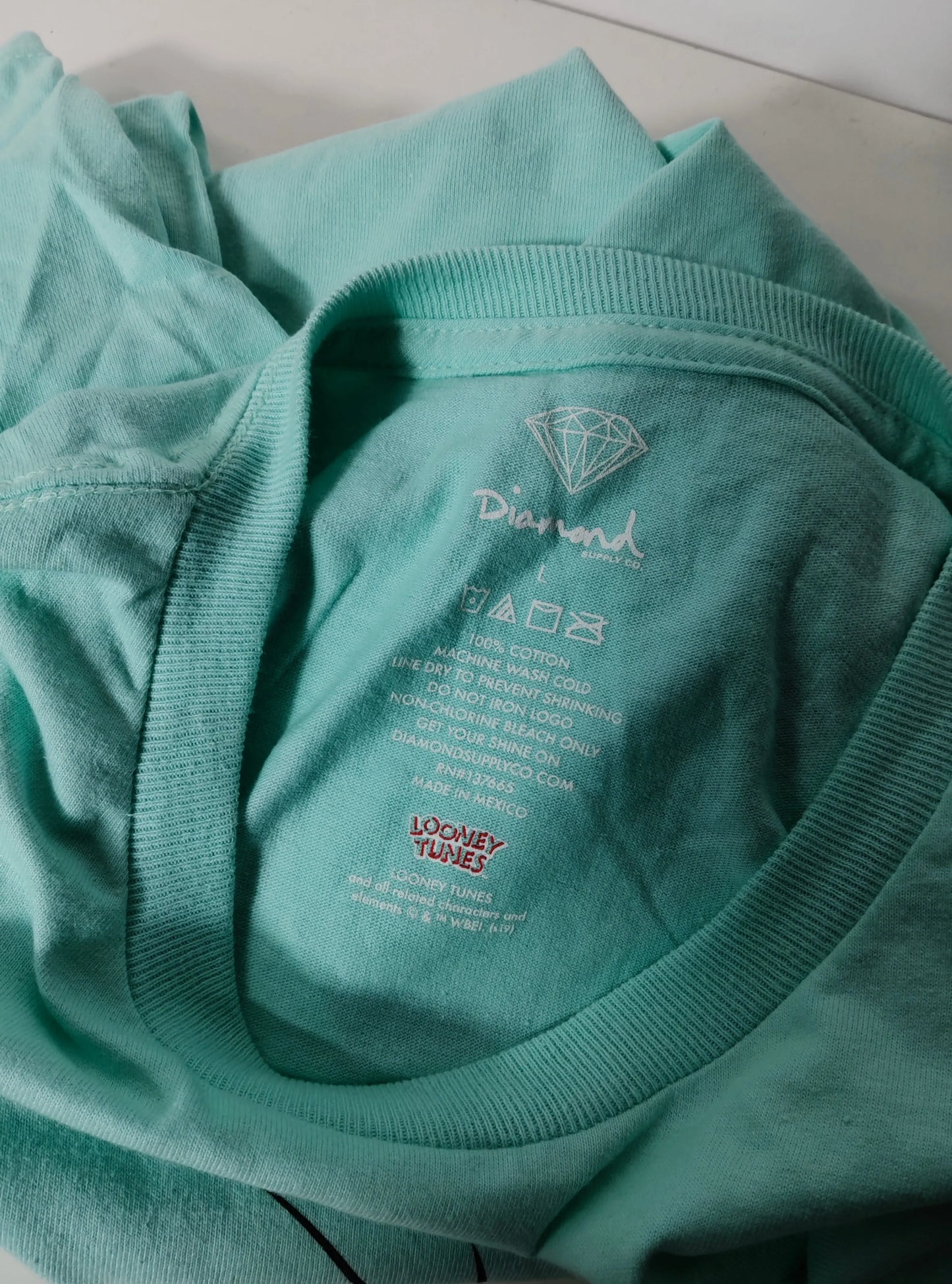 T-shirt bleu clair de Diamond Supply x Looney Tunes, avec étiquette d'entretien imprimée.
