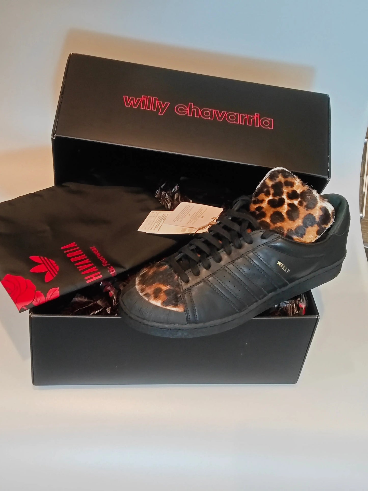 Basket noir à motif léopard par Adidas, avec le nom « Willy » sur le côté et une pochette noire avec un logo rouge.