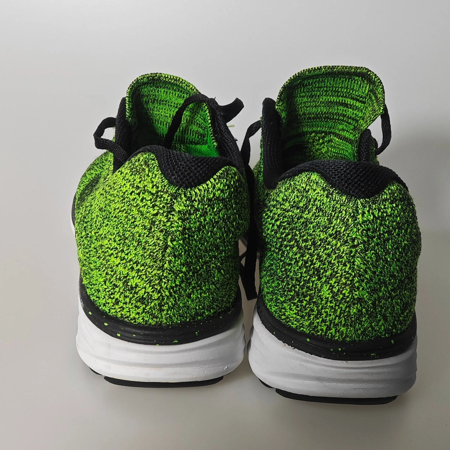 Baskets Flyknit vertes et noires Nike d'occasion, vue arrière montrant la texture tricotée et la semelle blanche.

