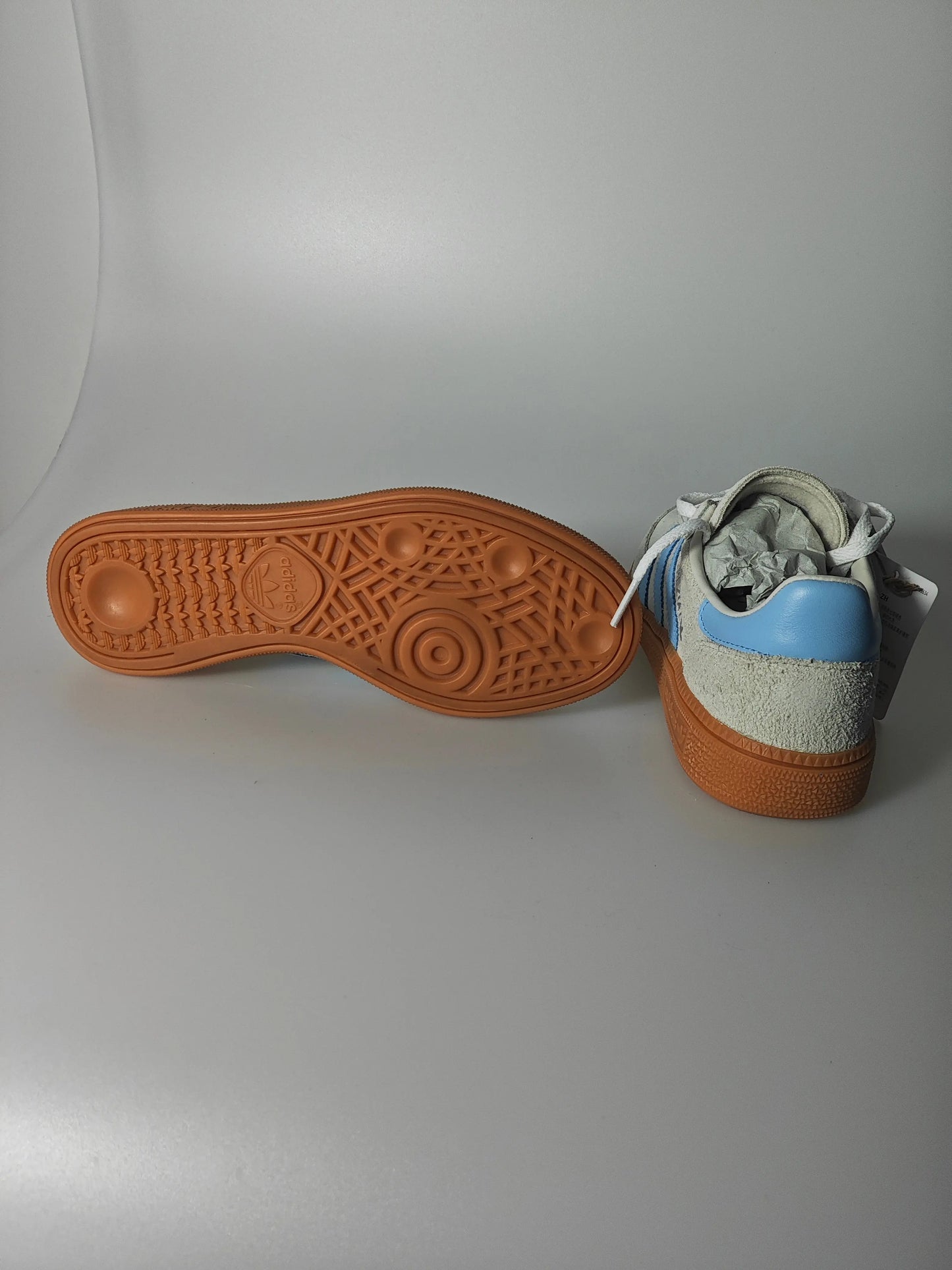 Basket en daim blanc et bleu, par Adidas, avec semelle extérieure marron en caoutchouc texturé.
