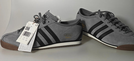 Baskets grises en daim de Adidas, avec trois bandes noires et semelles marron et blanche.
