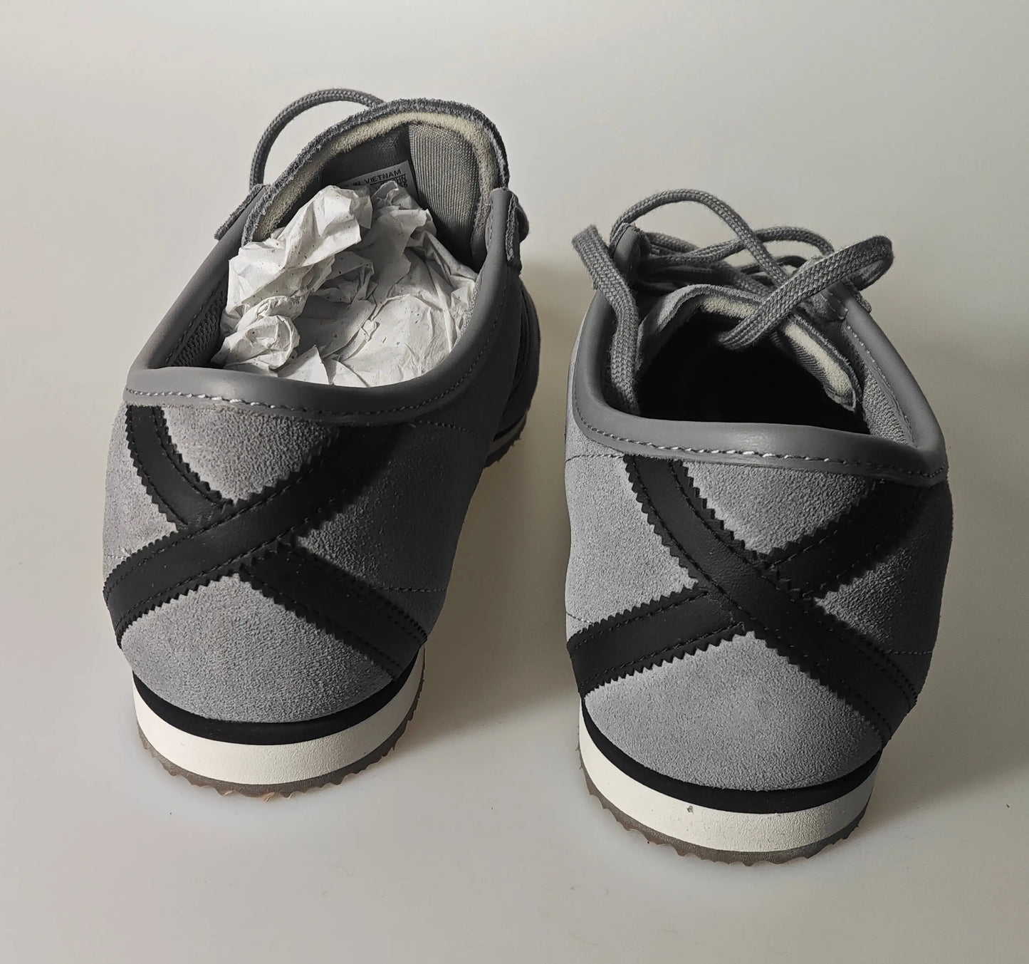 Baskets grises en daim de Adidas, avec des rayures noires en forme de croix à l'arrière.