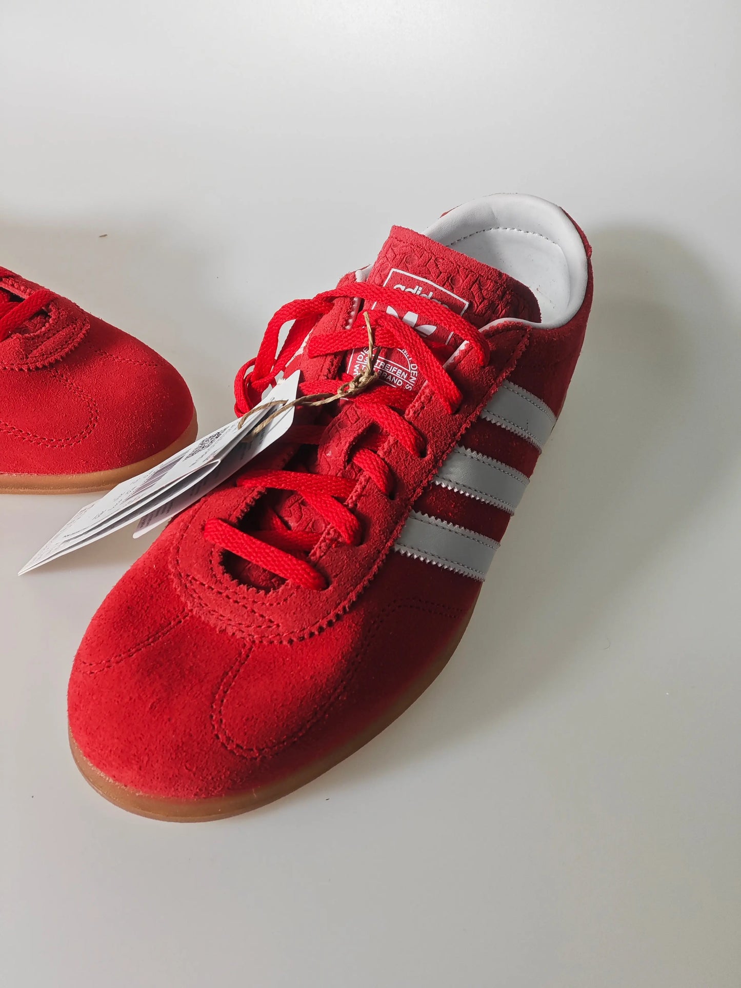 Basket rouge en daim Adidas avec trois bandes grises et lacets rouges.