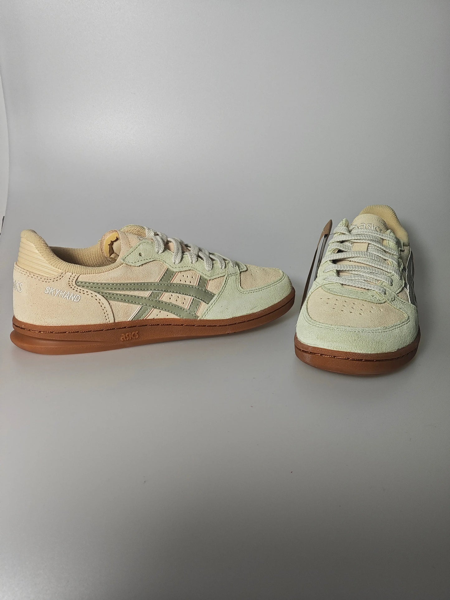 Chaussure de basket beige en daim, de Asics, avec des rayures vertes et une semelle marron.