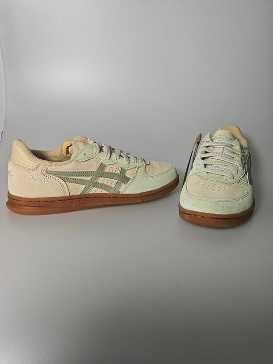Chaussure de basket beige en daim, de Asics, avec des rayures vertes et une semelle marron.