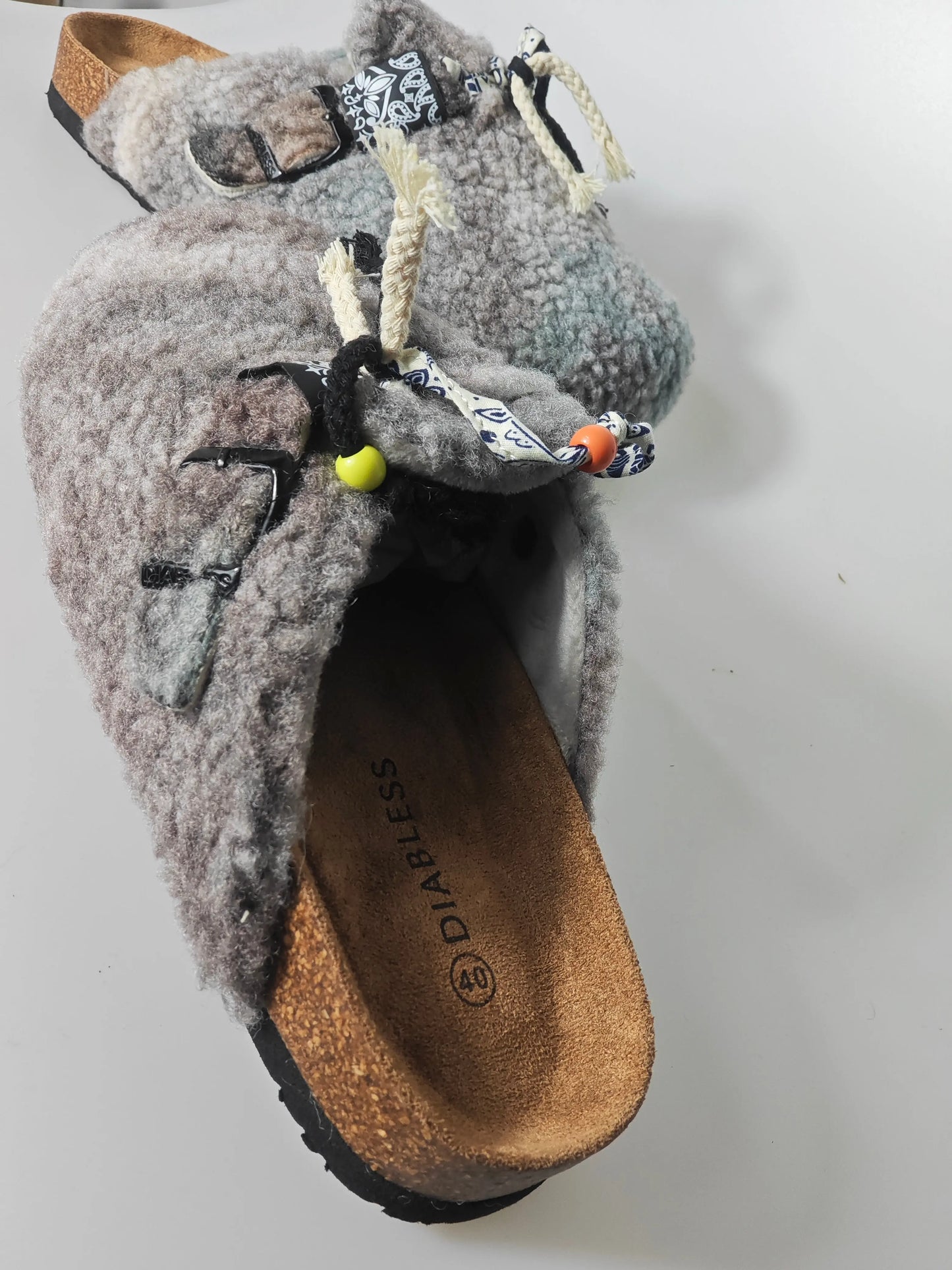Sabots fourrés gris de Diabless, avec détails de cordons décoratifs et boucle sur le dessus.
