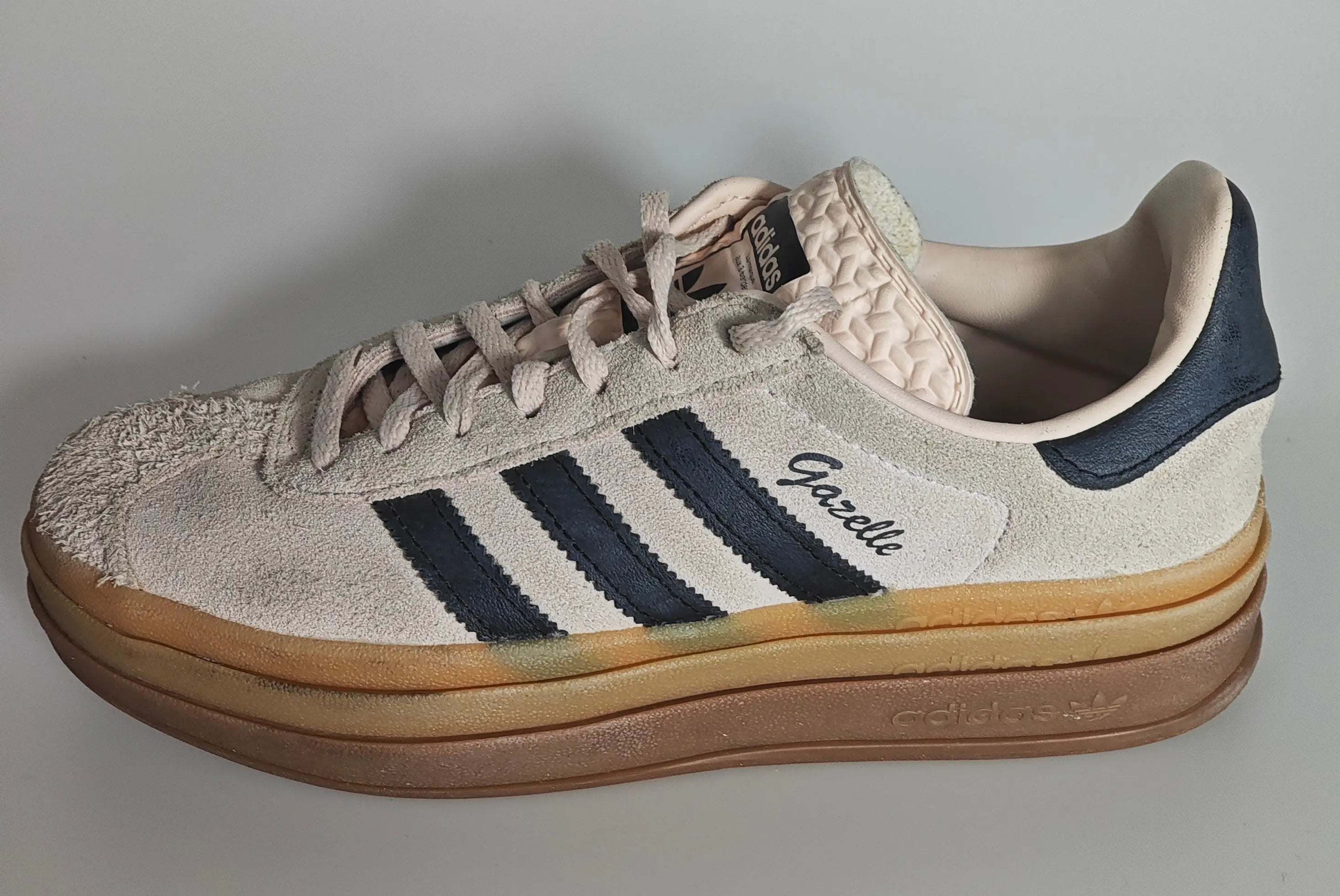 Baskets Gazelle beiges en daim premium d’Adidas, avec trois bandes noires et semelle épaisse marron.
