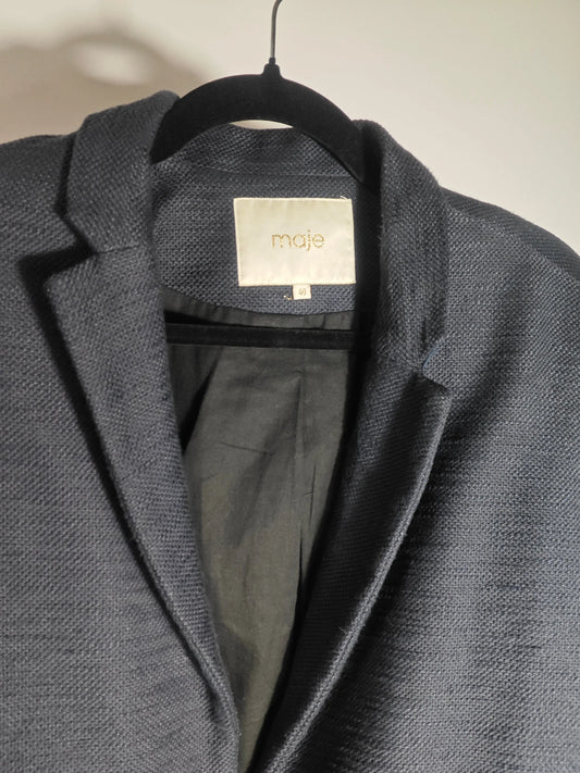 Manteau bleu marine Maje de seconde main, sur un cintre noir, avec doublure intérieure foncée.