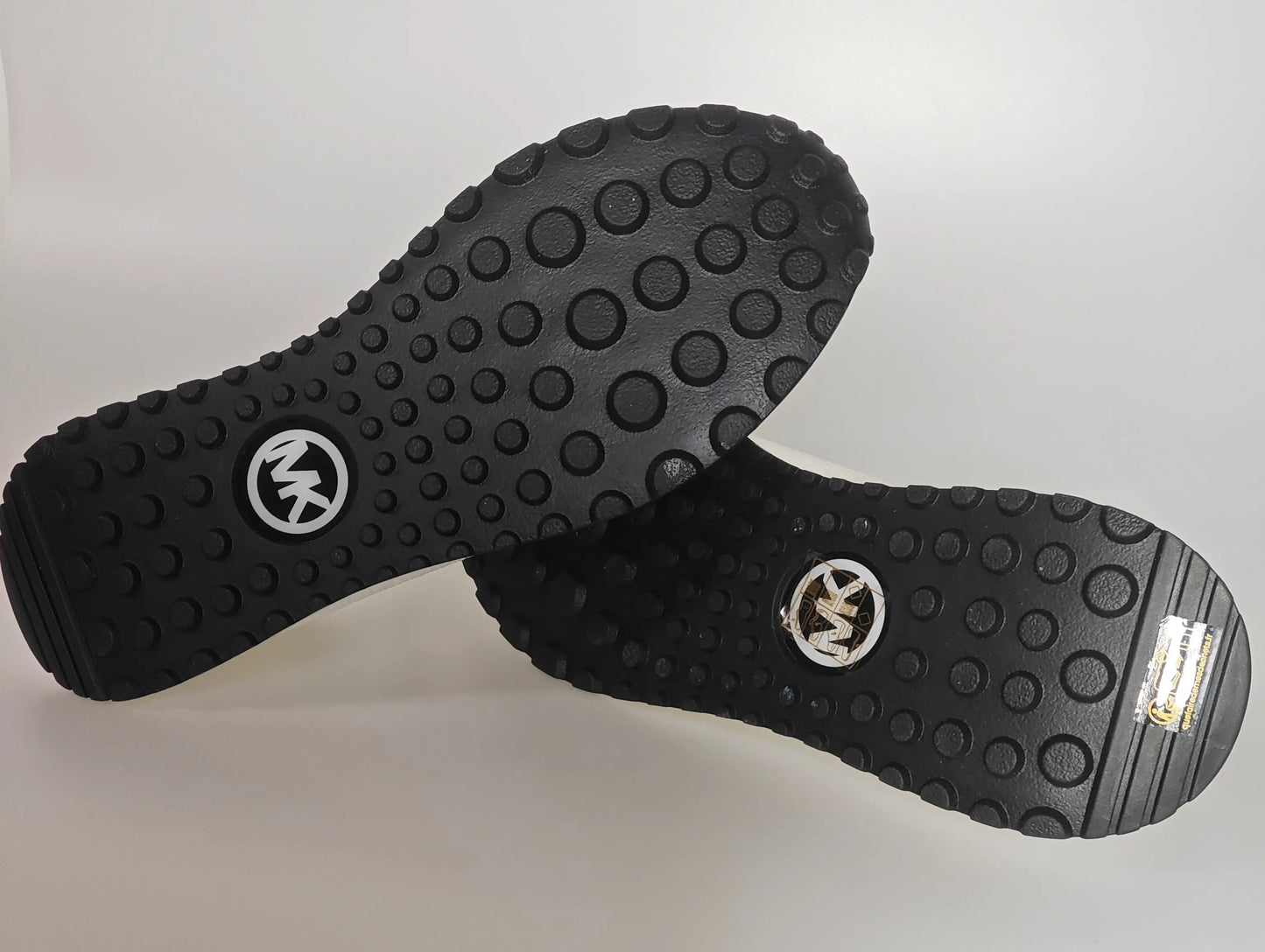 Semelles de sneakers noires à motif de cercles par Michael Kors avec logo visible.