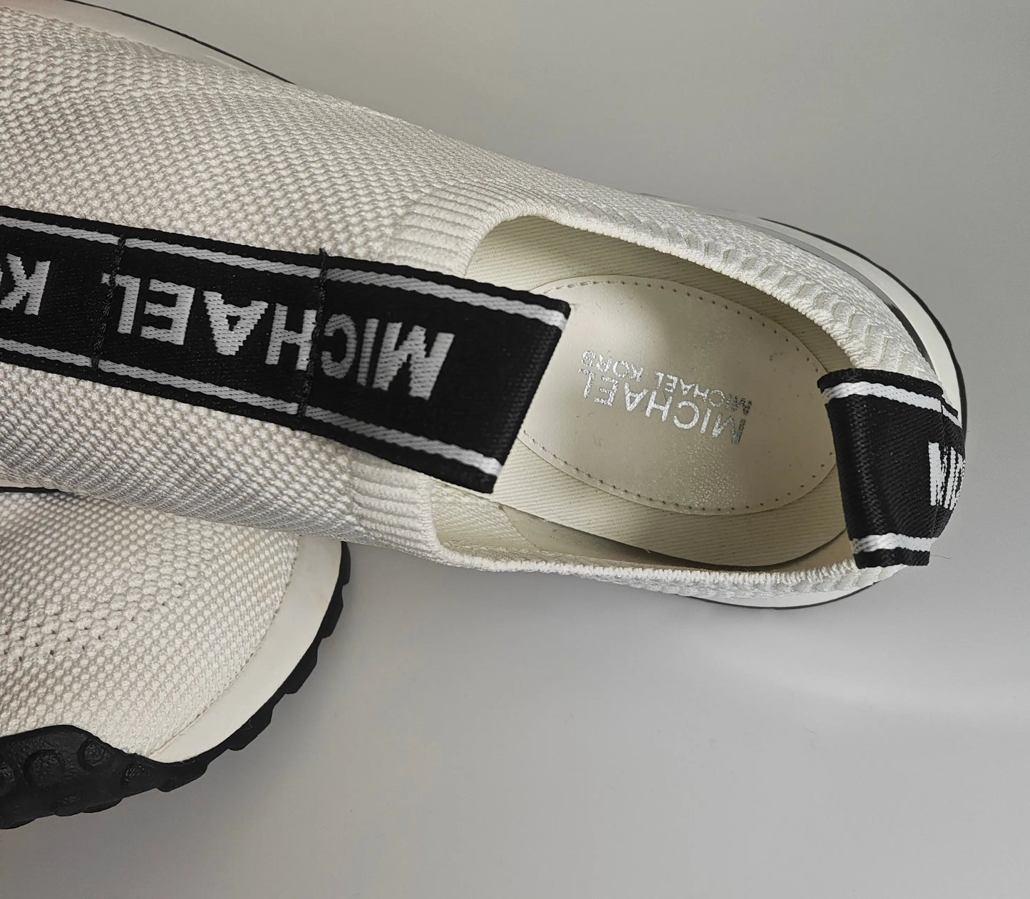 Espadrille en maille extensible blanche de Michael Kors, avec une bande élastique noire portant le logo.