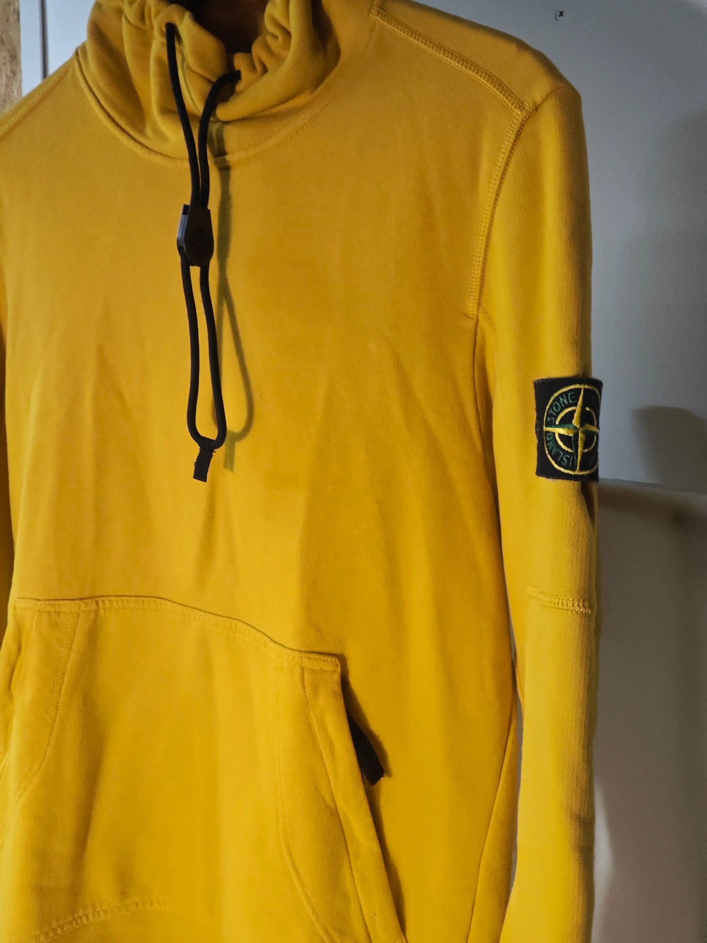 Sweat jaune Stone Island, avec capuche à cordon noir et poche kangourou, orné d'un écusson sur la manche.
