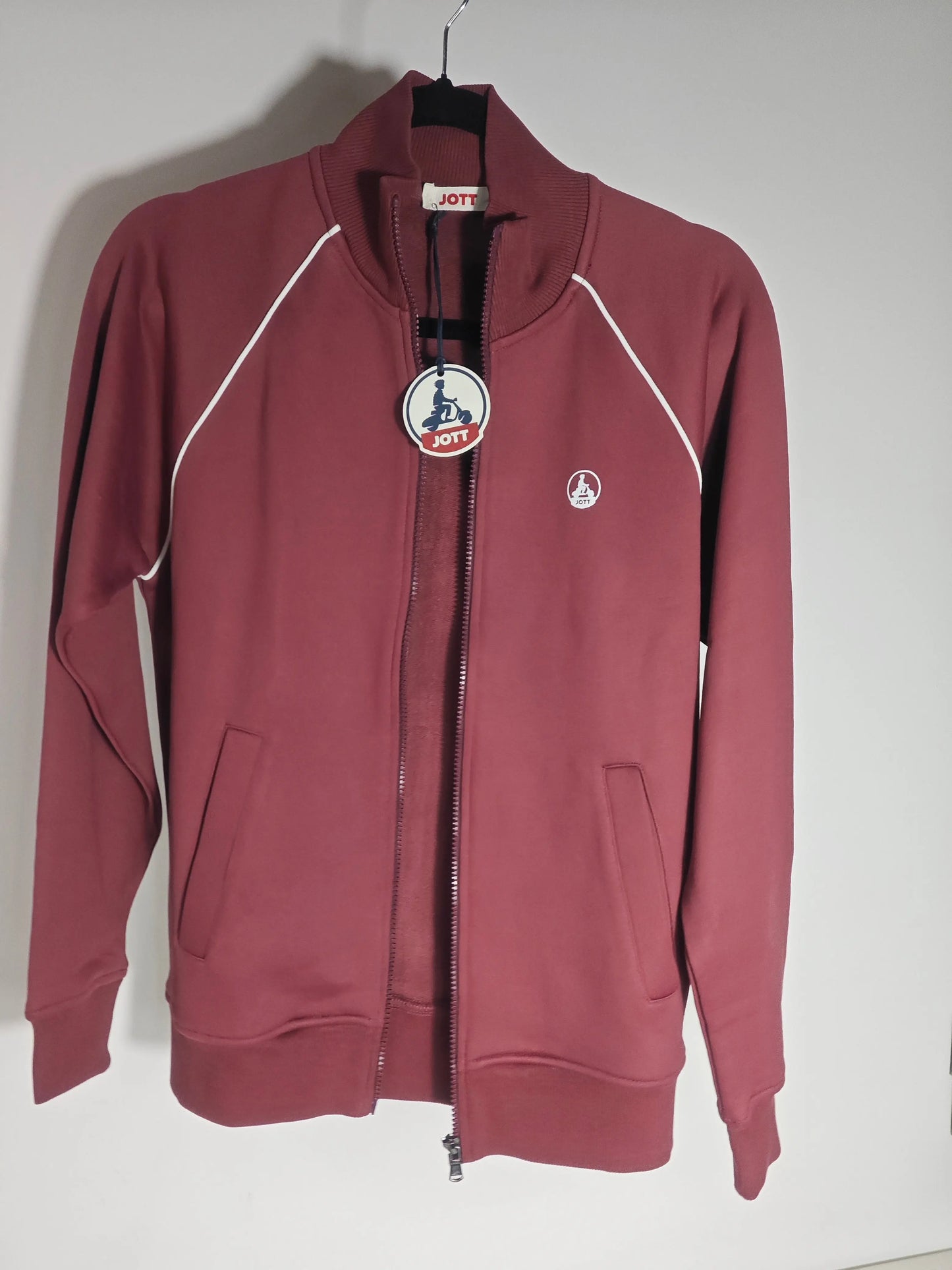 Veste de survêtement zippée bordeaux de Jott, avec une bande blanche contrastante sur les manches et poches avant.