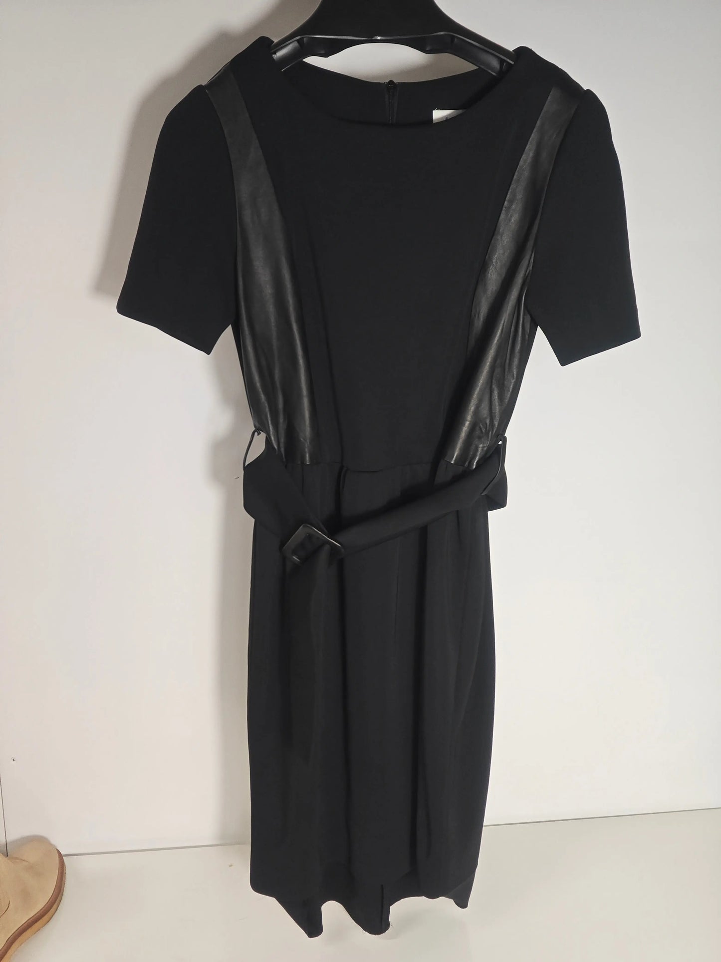 Robe noire avec empiècements en similicuir de Sandro, coupe mi-longue, ceinture тон-sur-тон et manches courtes.
