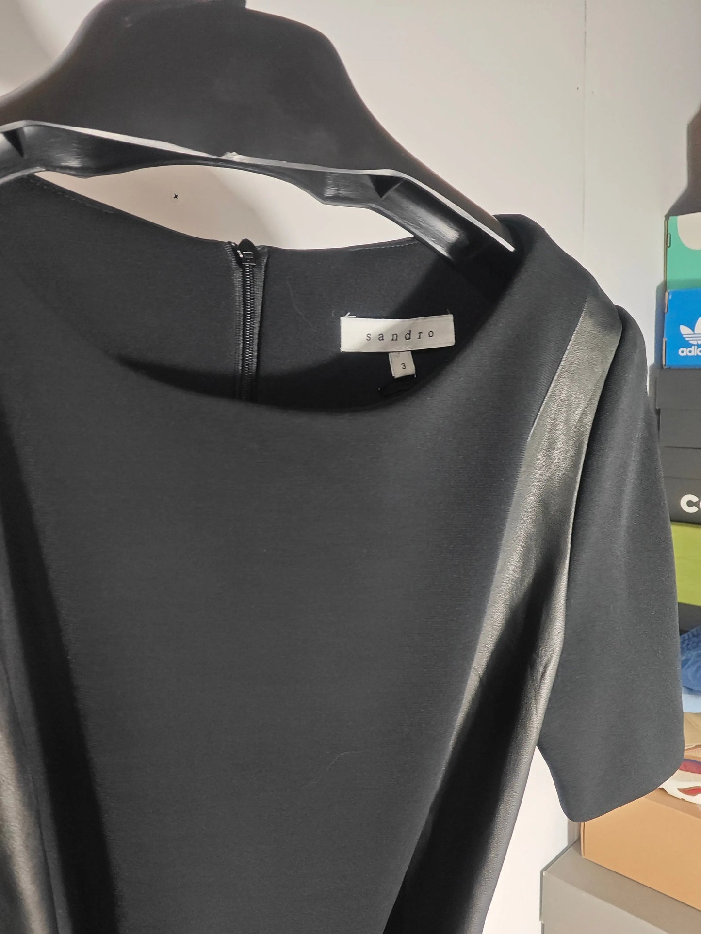 Robe noire par Sandro, avec fermeture éclair dans le dos et détail en cuir sur l'épaule.
