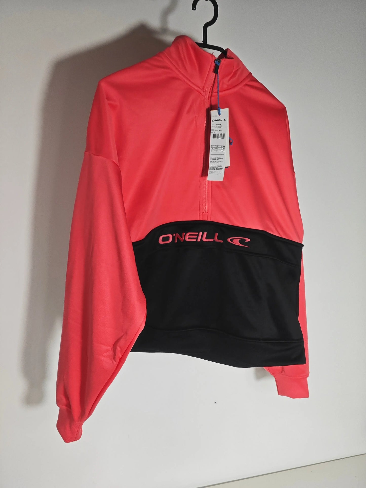 Veste corail et noire taille S de O'Neill suspendue à un cintre, avec étiquette.
