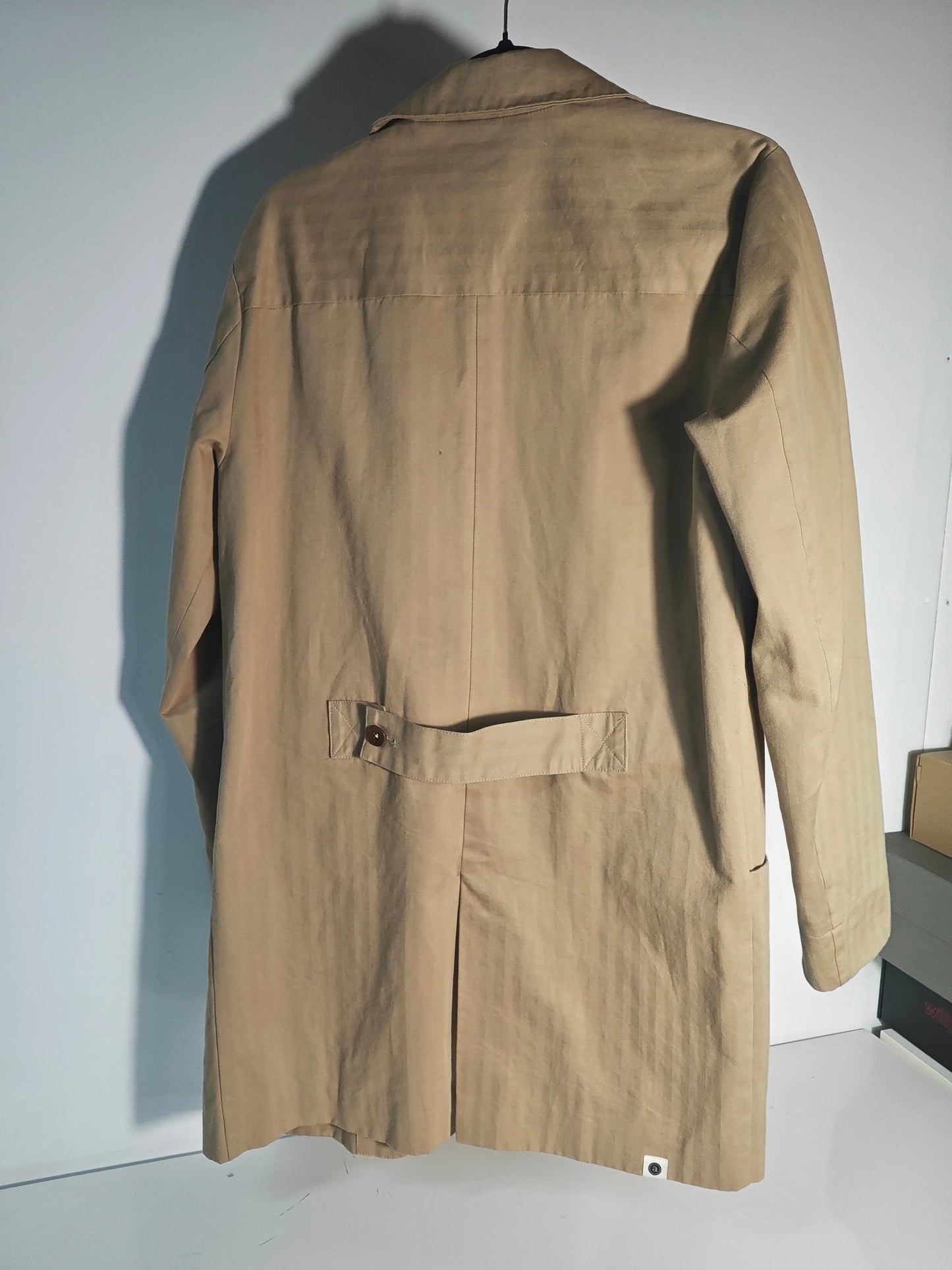 Manteau trench couleur sable Anerkjendt, coupe mi-longue avec patte de boutonnage au dos.
