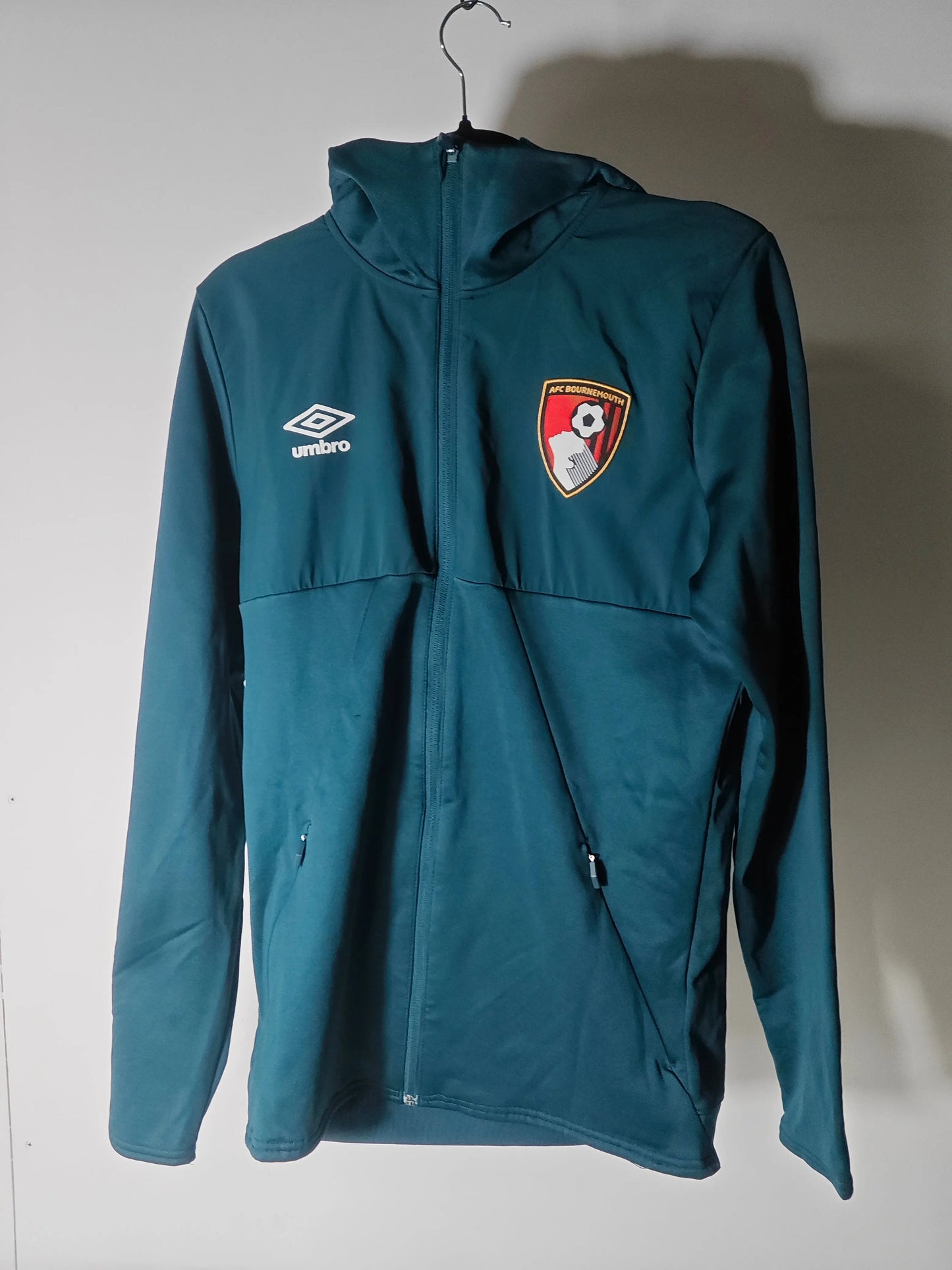 Veste de survêtement bleu marine par Umbro avec écusson de l'AFC Bournemouth, suspendue à un cintre.
