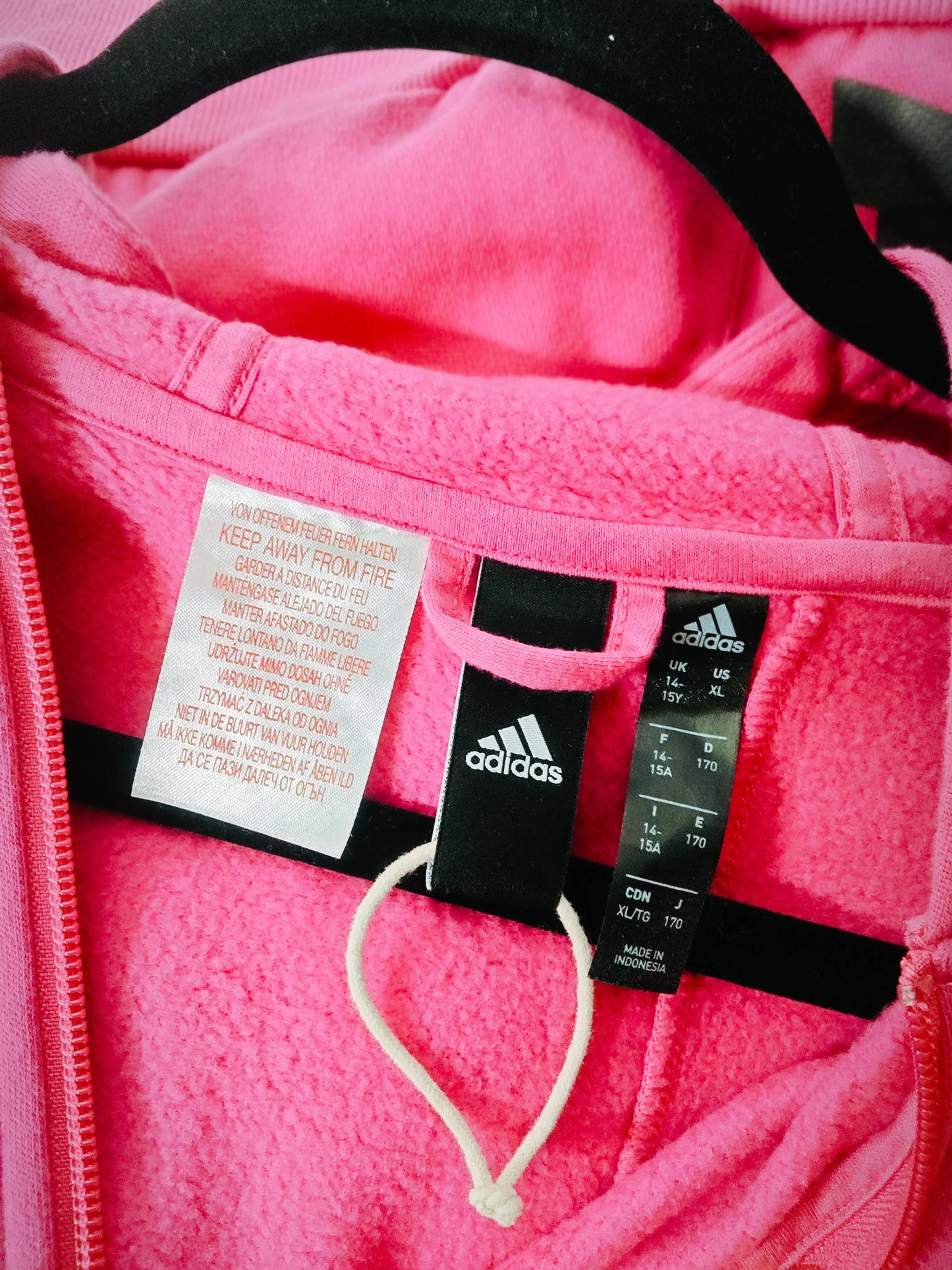 Sweat à capuche rose fuchsia de Adidas, avec étiquettes d'avertissement de sécurité, sur un cintre.

