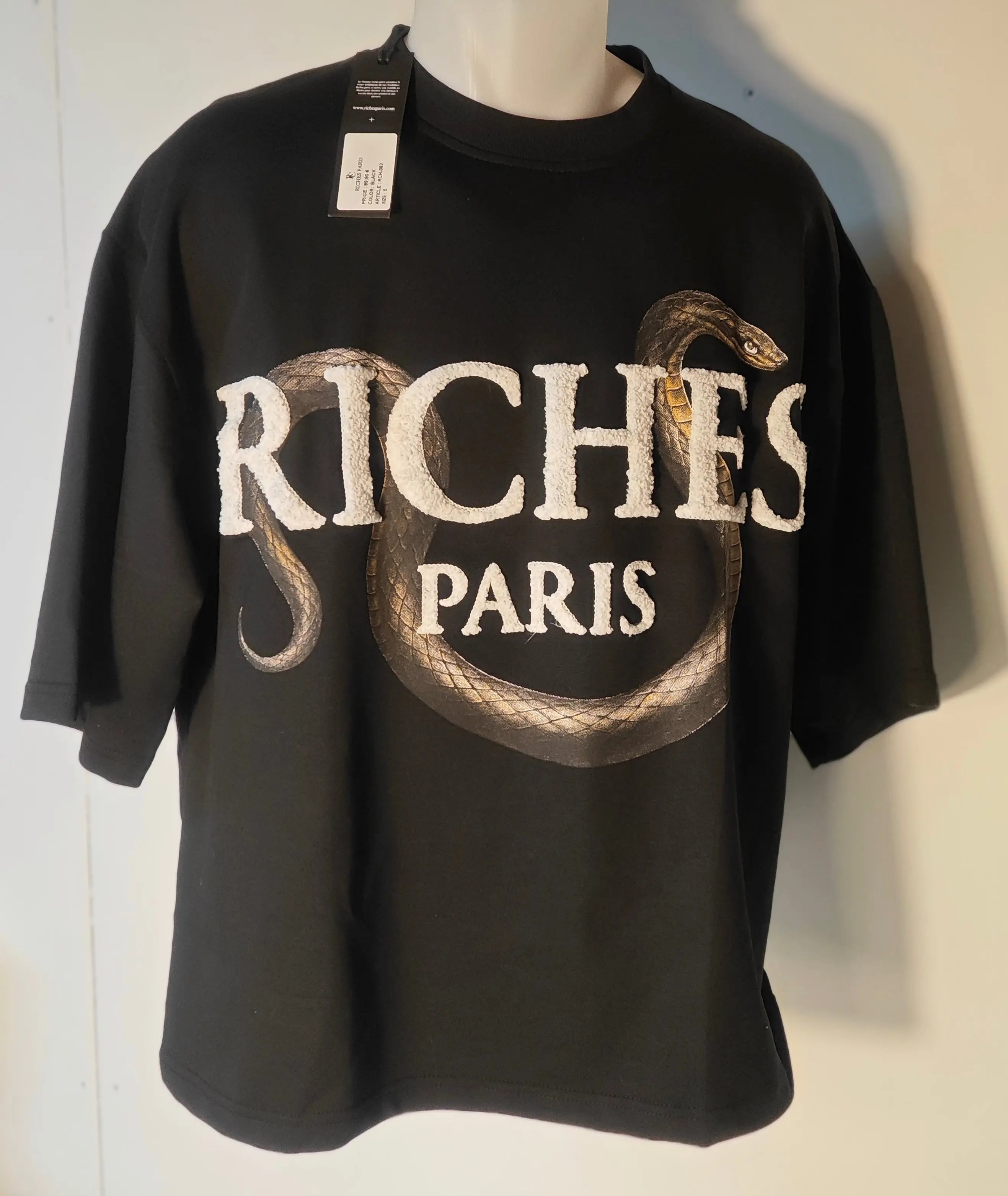 T-shirt noir Riches Paris avec motif serpent enroulé autour du lettrage blanc.
