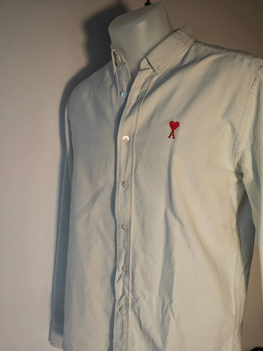 Chemise à rayures blanches et bleues by AMI, avec un logo cœur rouge sur la poitrine, portée sur un mannequin.