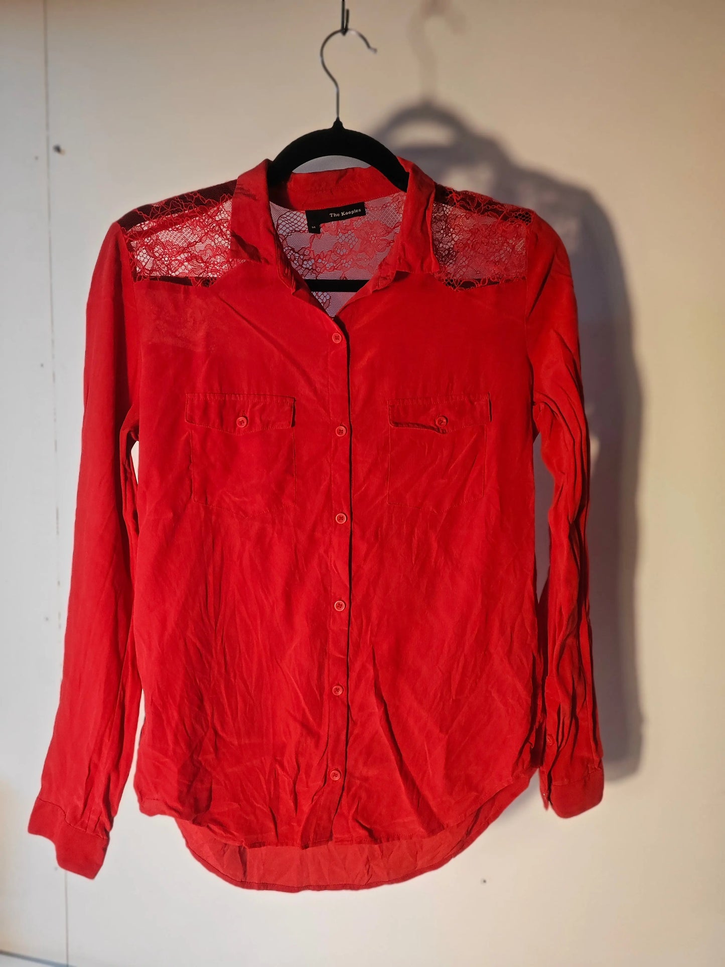 Chemise en soie rouge par The Kooples, avec empiècements en dentelle aux épaules et poches poitrine boutonnées.