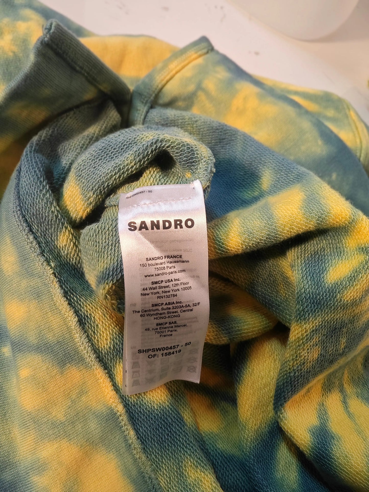 Sweat à capuche tie and dye bleu et jaune de Sandro, présentant une étiquette de marque blanche visible.

