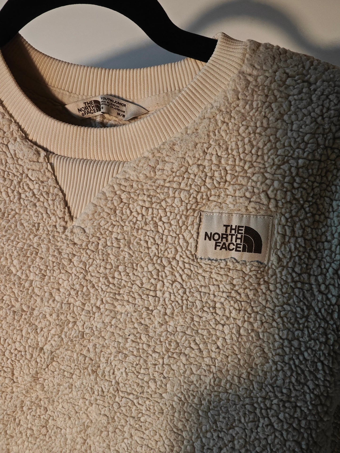 Pull en polaire sherpa beige de The North Face, avec col côtelé et logo carré.
