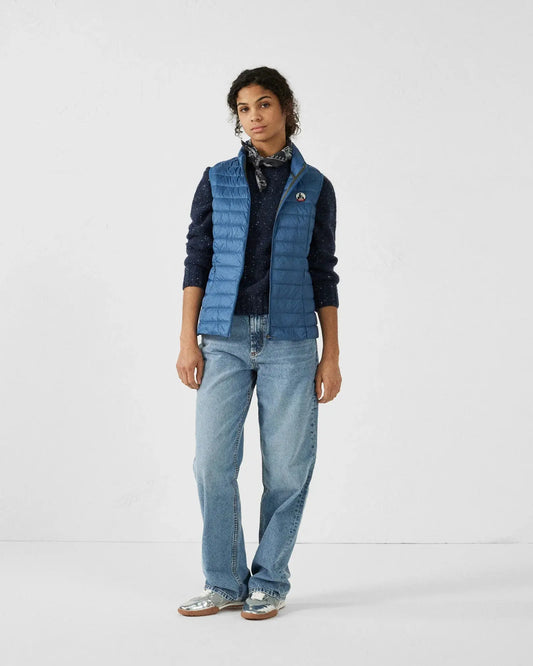 Doudoune sans manches bleue en jean de Jott, portée sur un pull bleu foncé et un foulard à motifs.