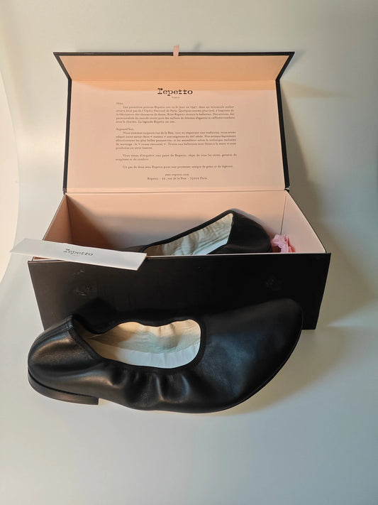 Ballerines noires en cuir de Repetto avec leur boîte, présentées à plat.
