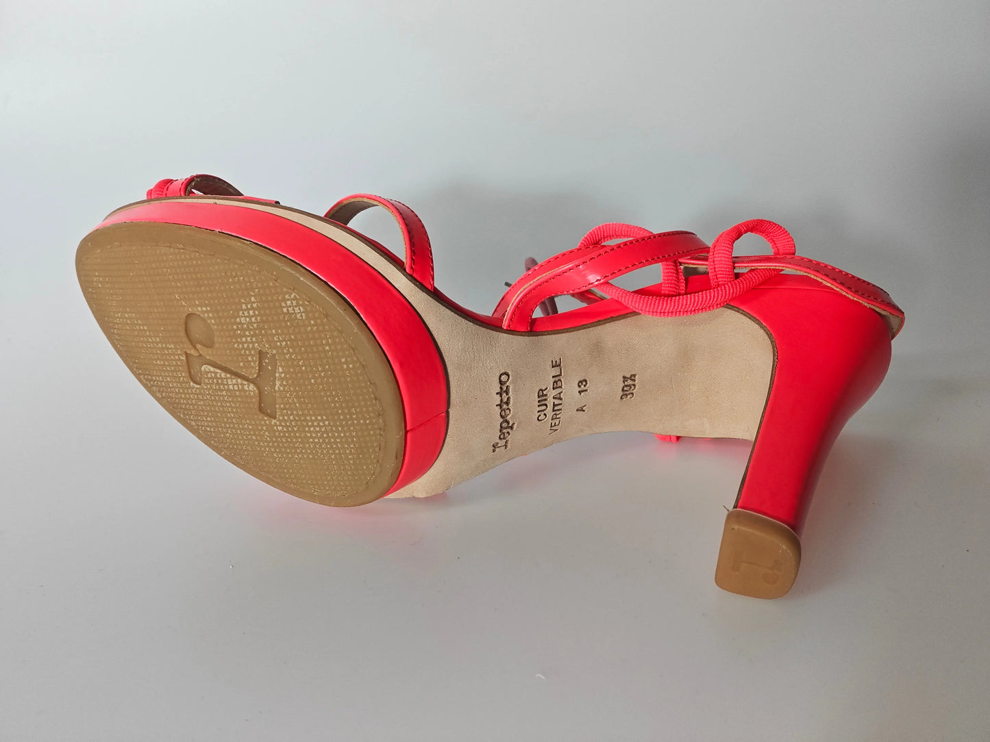 Sandale à talon rouge verni de Repetto, avec semelle texturée et brides entrecroisées.
