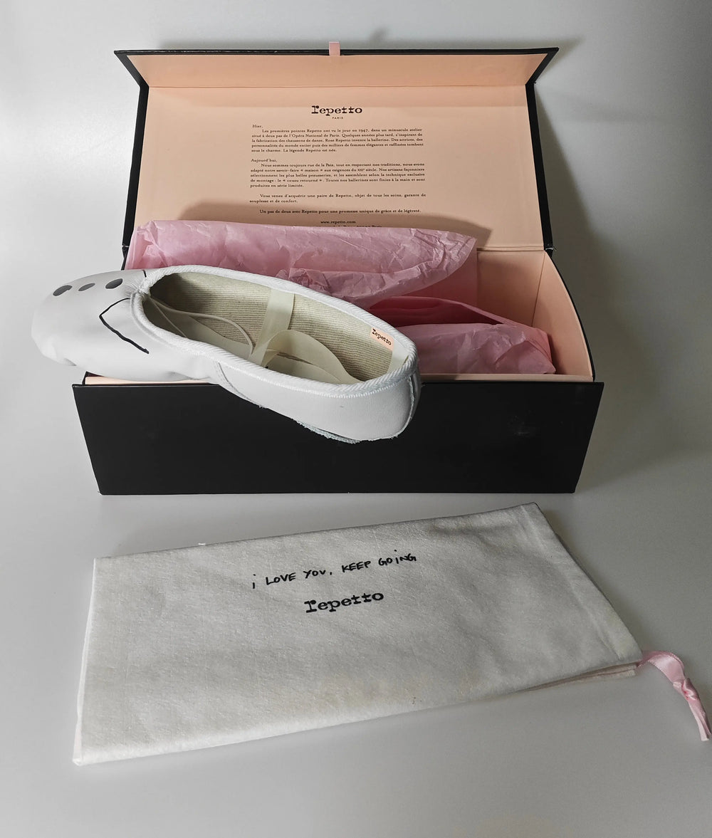 Ballerines blanches de Repetto, présentées dans leur boîte avec papier de soie rose et pochon en tissu.
