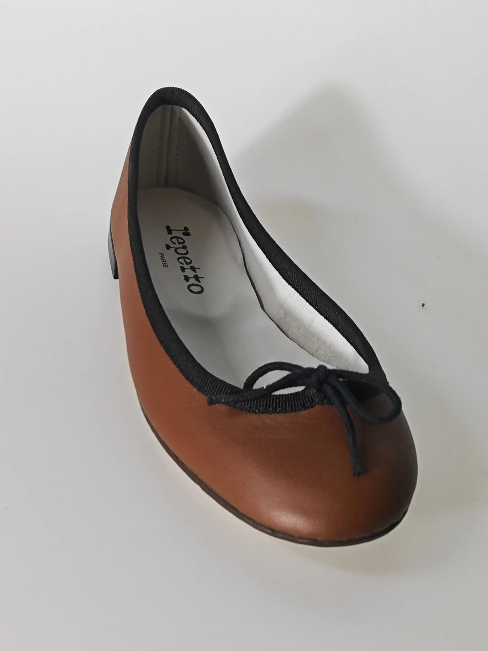 Ballerine marron en cuir de Repetto, avec bordure noire et petit nœud décoratif sur le dessus.
