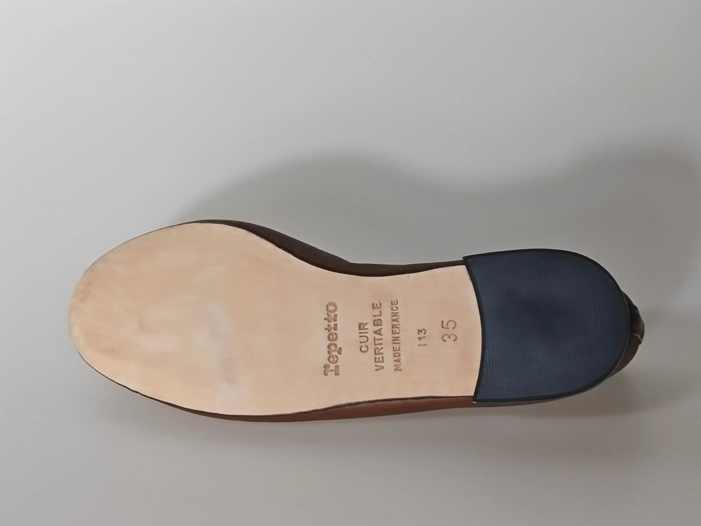 Ballerine marron en cuir de Repetto, montrant la semelle lisse avec talon bleu marine.
